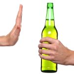 A hand held up to a green bottle of liquid being offered by another person.